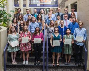 A group of students stand holding paper. 