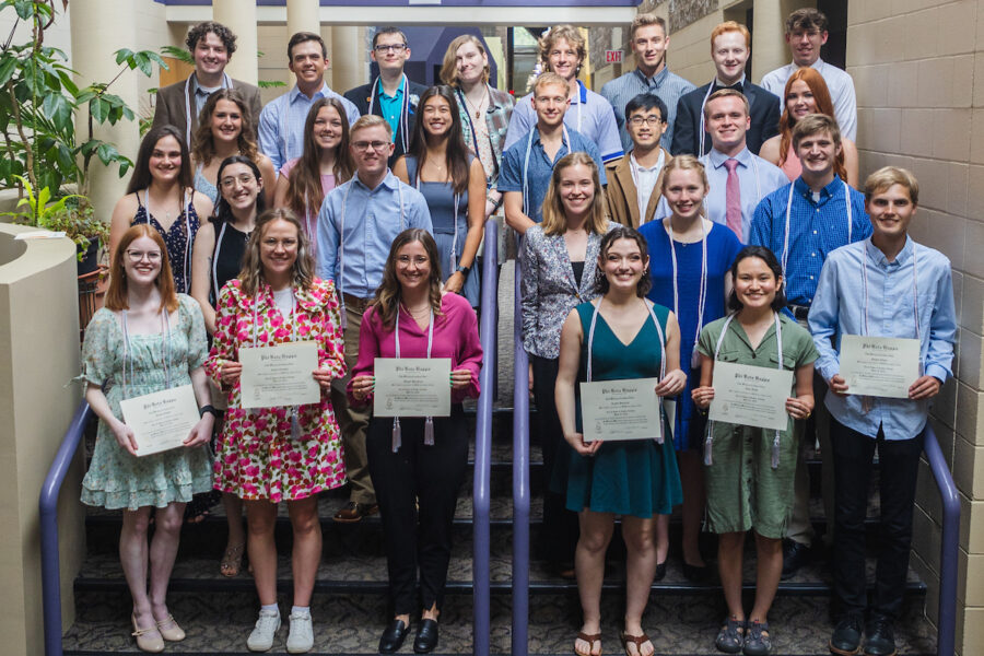 A group of students stand holding paper.