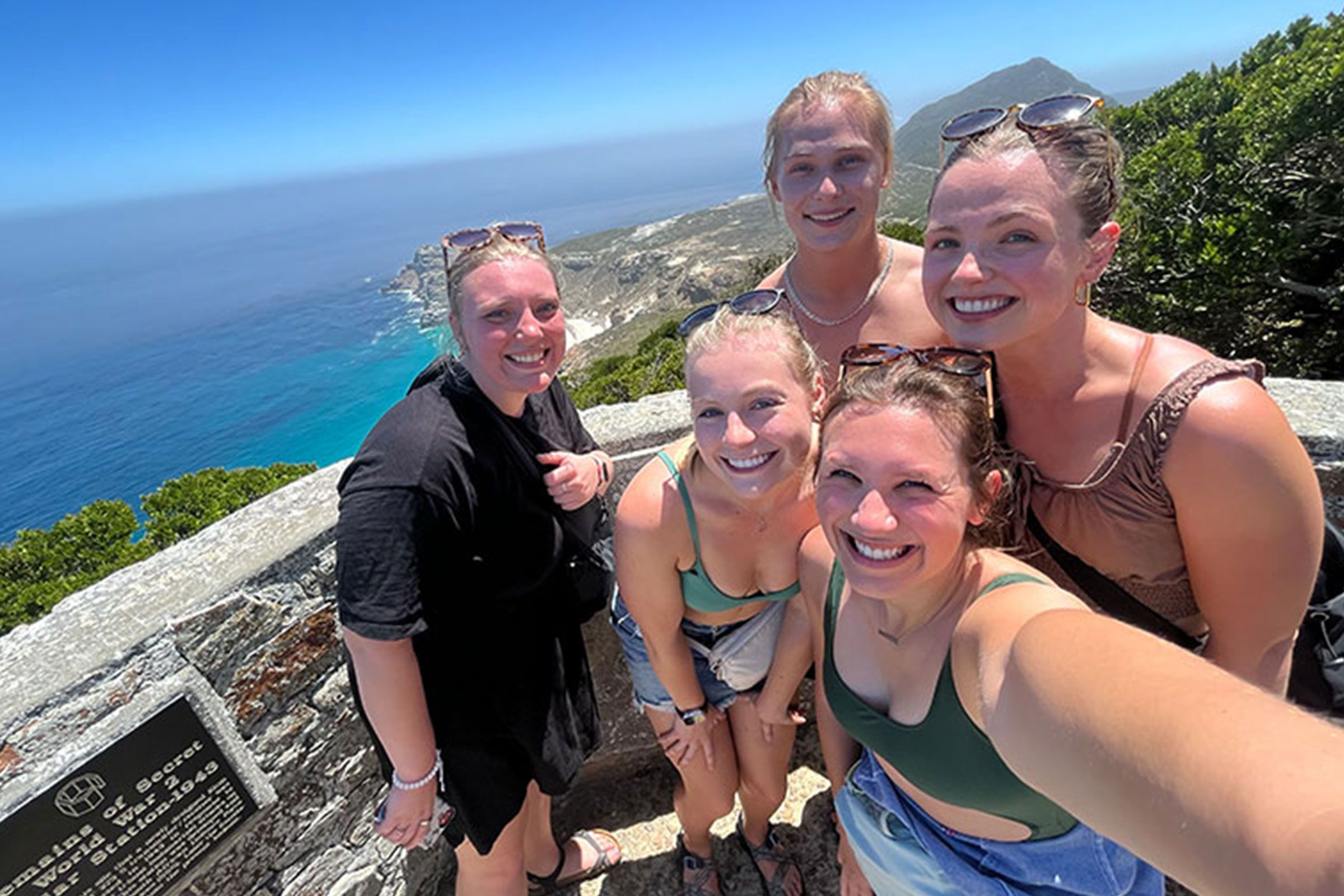 A group of women posing on an overlook with an ocean behind them