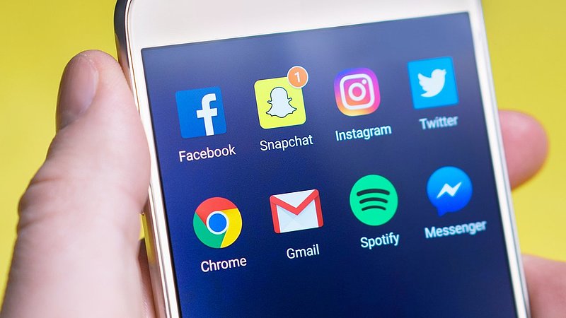 person is holding a apple phone with popular media apps on the screen