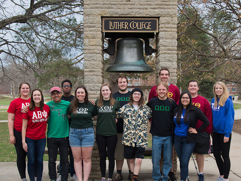 various student organization and club members stand in front of the Luther bell