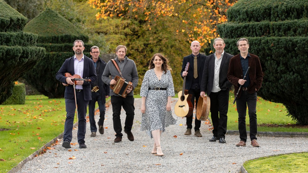 Seven person music group, Danú, walking down a wooded path with their instruments