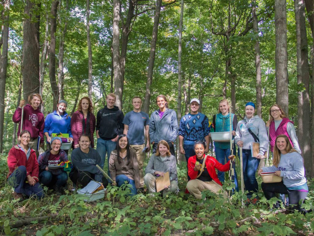 Two rows of people stand in the woods.