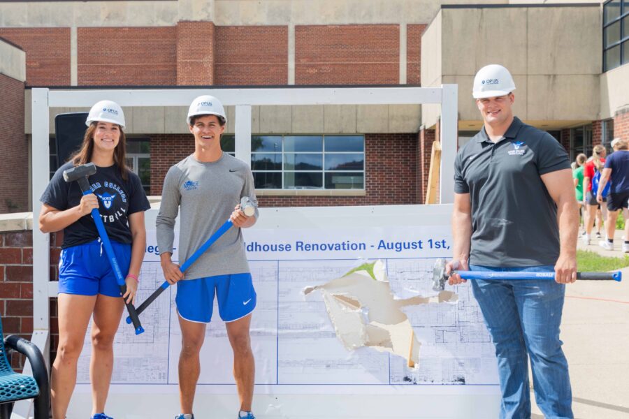 3 students wearing hard hats and holding sledgehammers