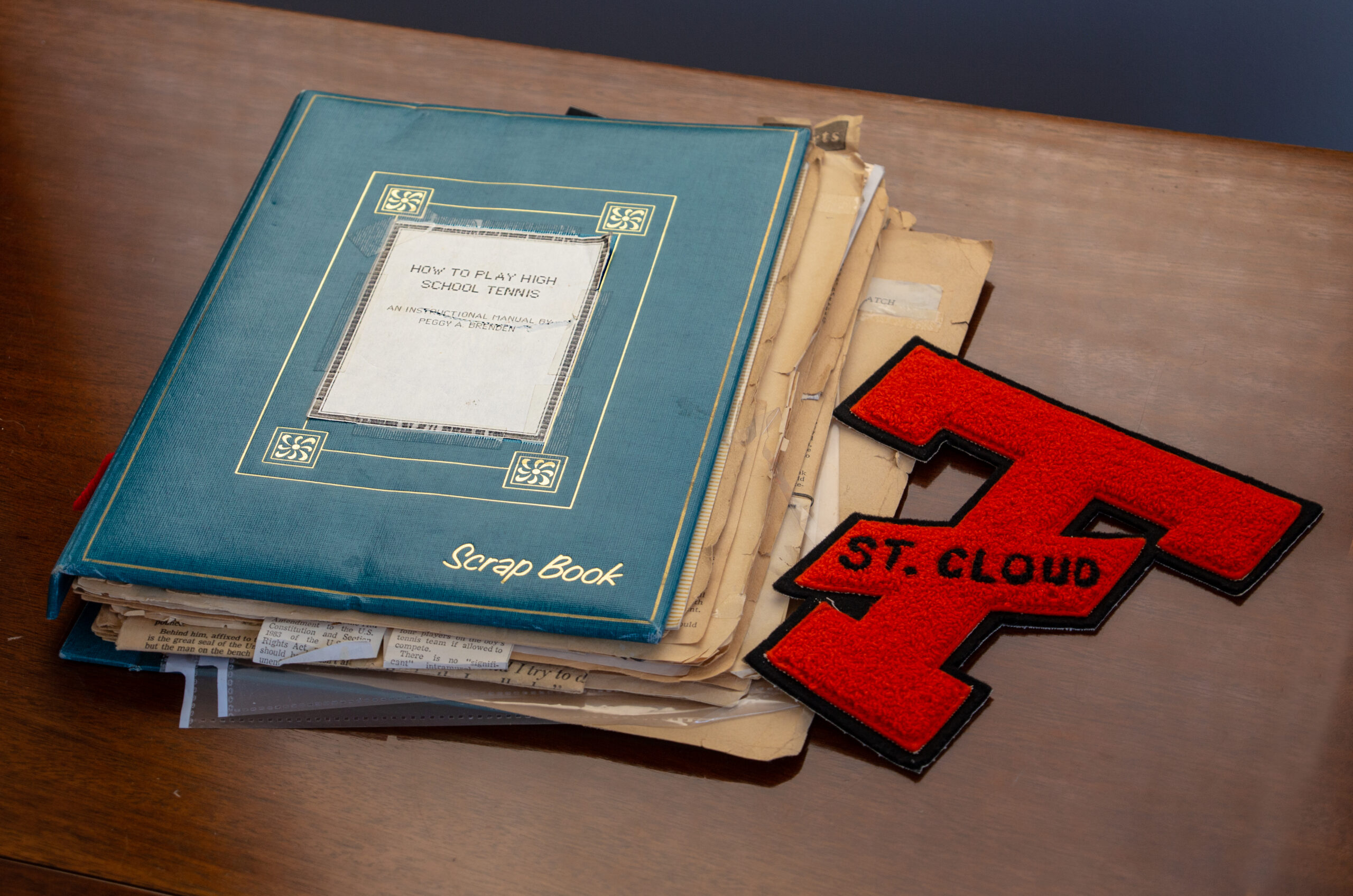An overfull vintage-looking scrapbook next to a red high-school varsity sports letter T