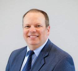 head shot of Mike Grimm, in blue-grey suit and navy tie, smiling