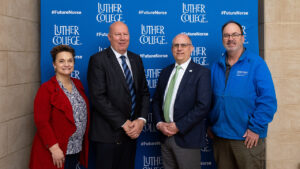 four people stand in front of a Luther College backdrop