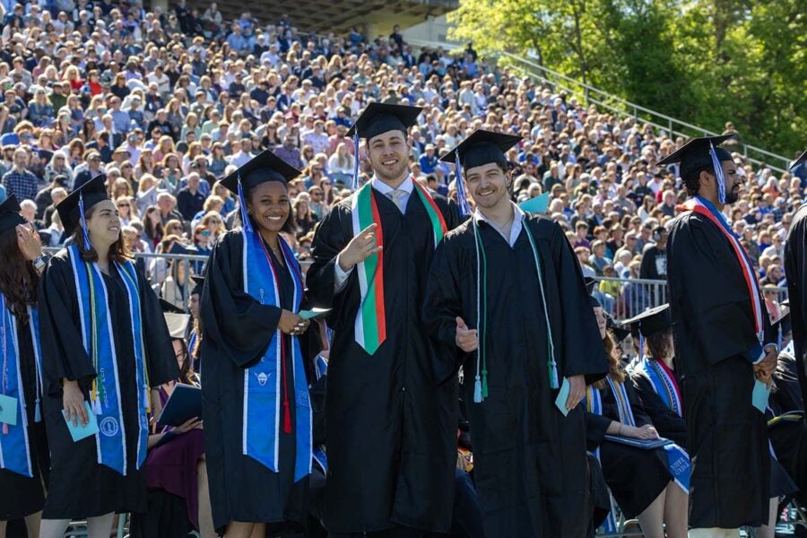 Students smile in front of a huge crowd at graduation day.