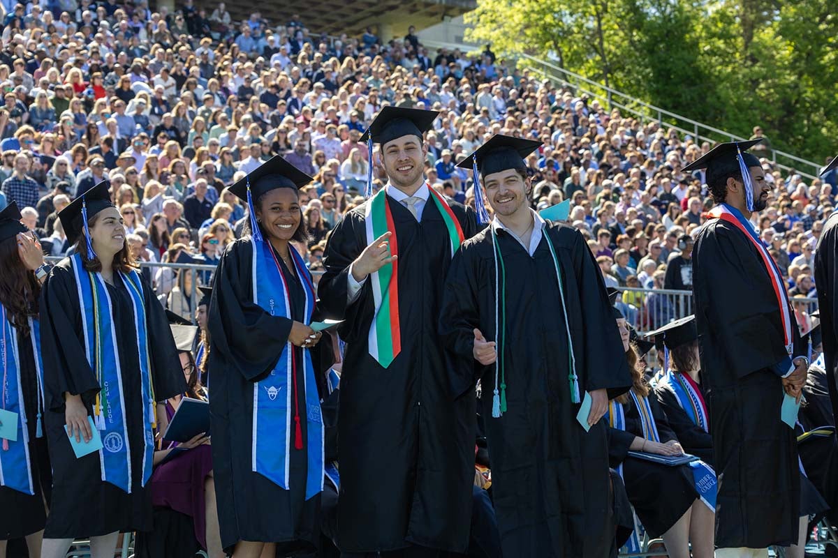 Students smile in front of a huge crowd at graduation day.