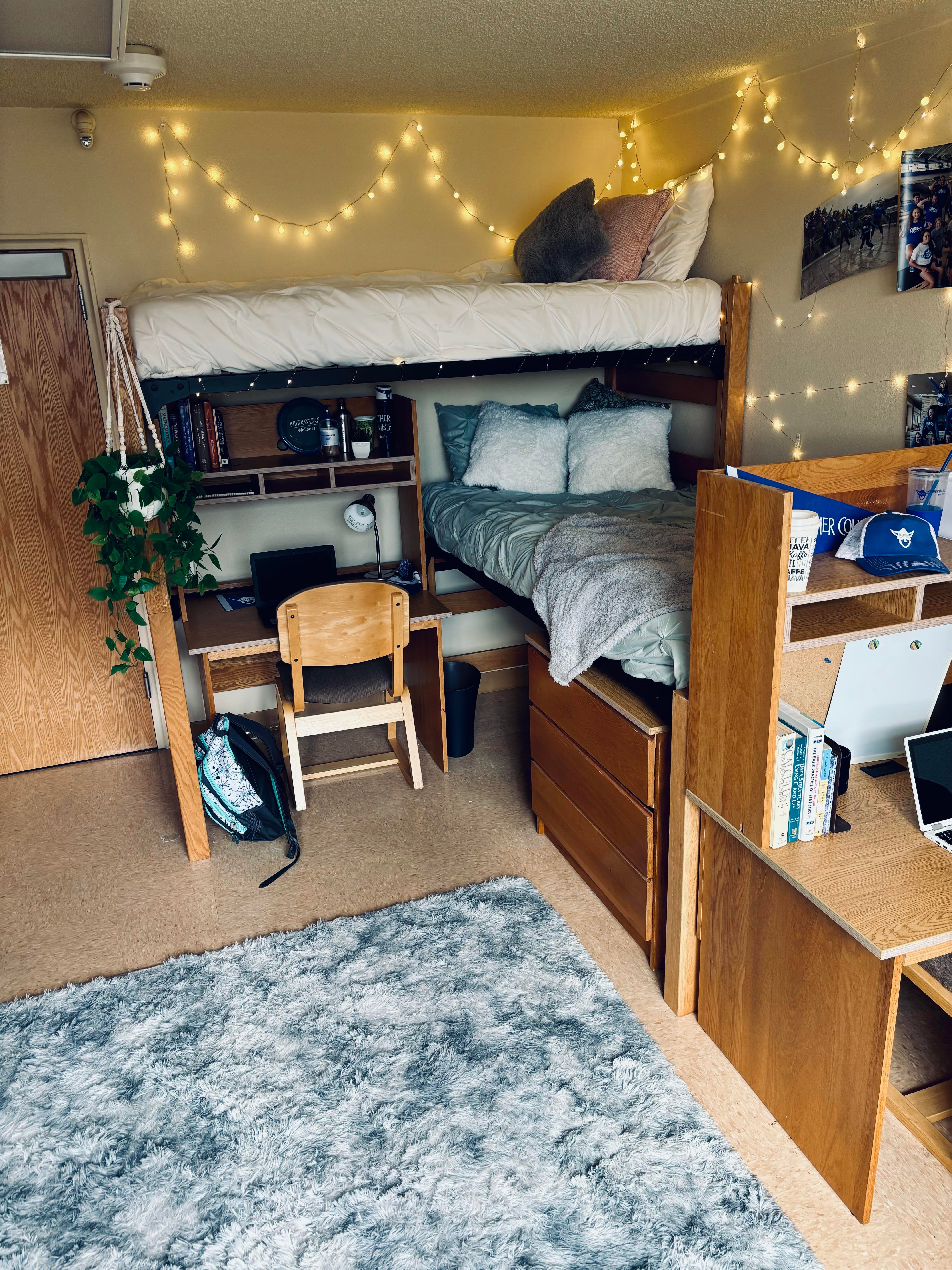 Students sit on a couch and on the bed in a dorm room, laughing and eating snacks.