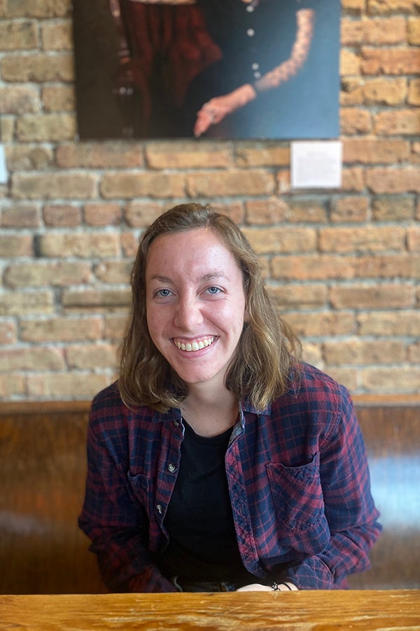 Kirsten Loynachan ’22 sits at a table with a photograph and a brick wall behind her