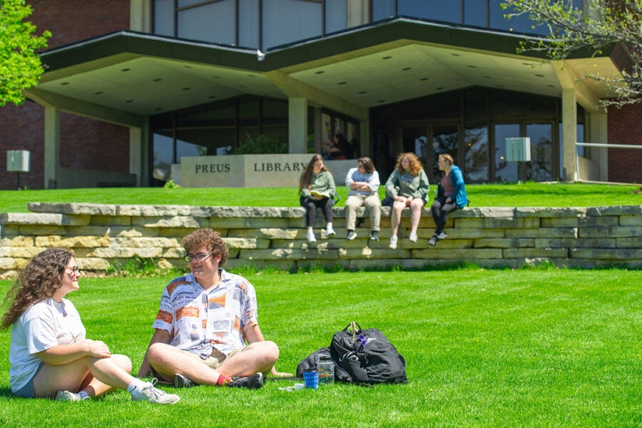college students sit on lawn in front of library