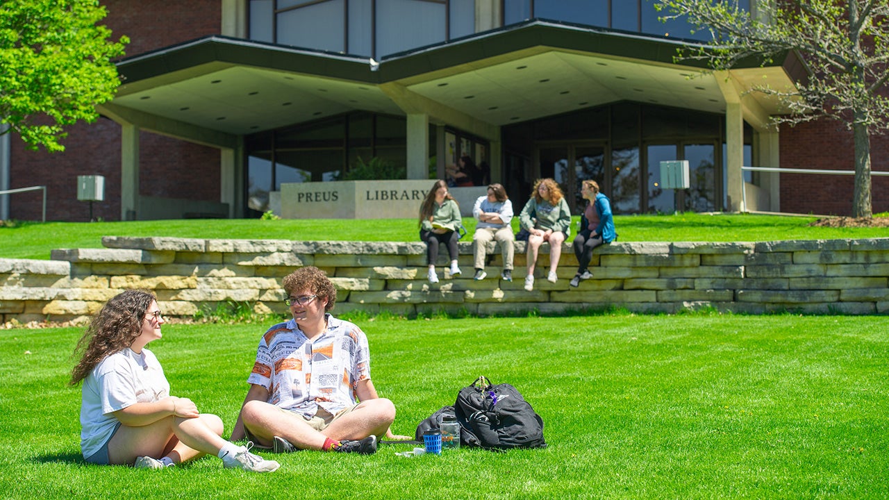 college students sit on lawn in front of library