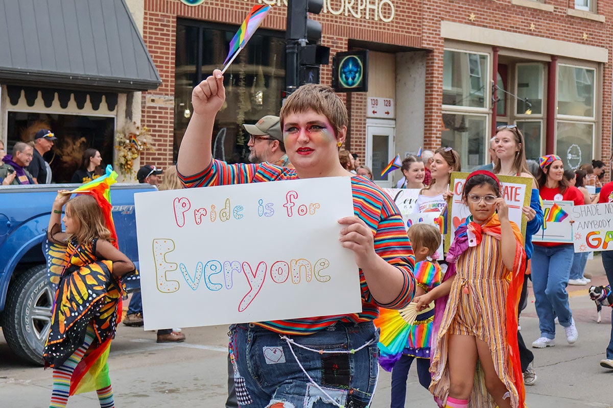 Person in a pride parade holding a sign that says "Pride is for Everyone."