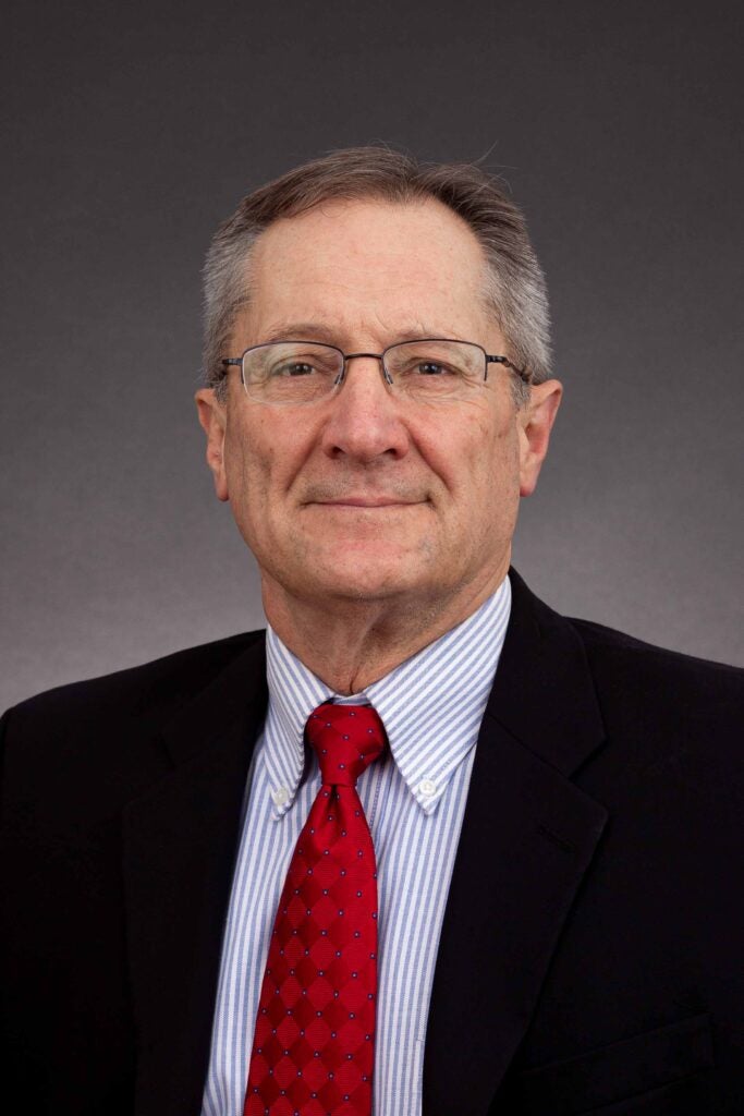 Portrait of Rob Larson wearing a black suit jacket and red tie