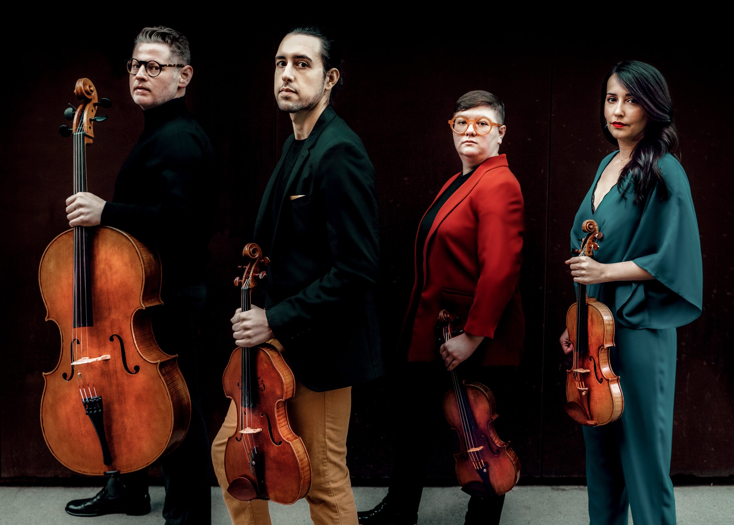 The members of Catalyst Quartet in front of a black backdrop holding their stringed instruments