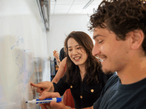 Marketing professor teaching a student at whiteboard