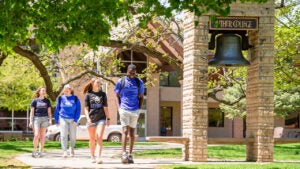 students walk past the Luther College bell on a sunny spring day