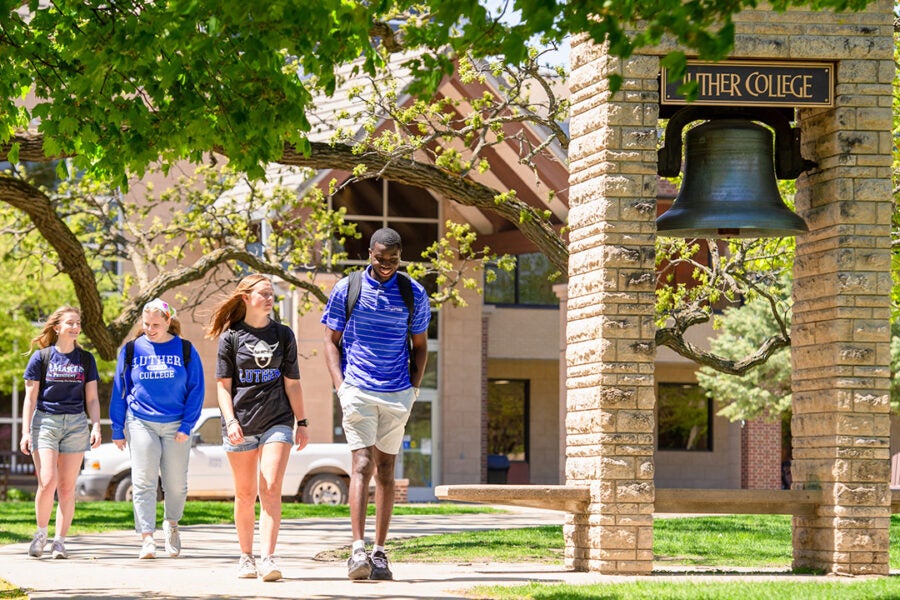 students walk past the Luther College bell on a sunny spring day