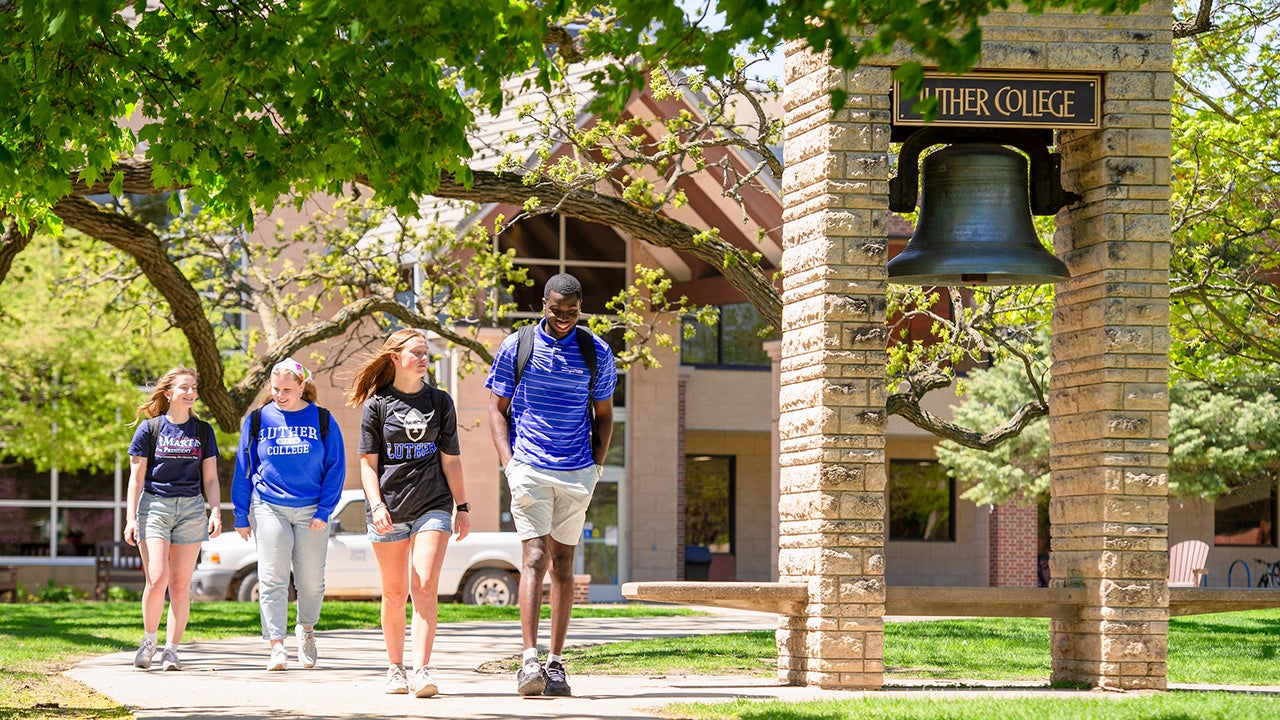 students walk past the Luther College bell on a sunny spring day