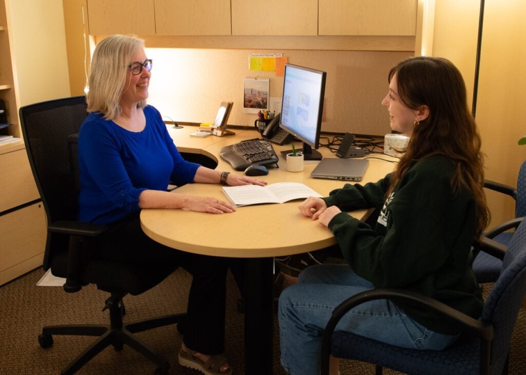 An advisor and a student sit together at a desk.
