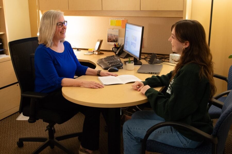 An advisor and a student sit together at a desk.