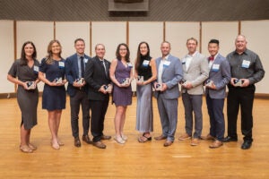 Eleven people stand on the stage holding awards. 