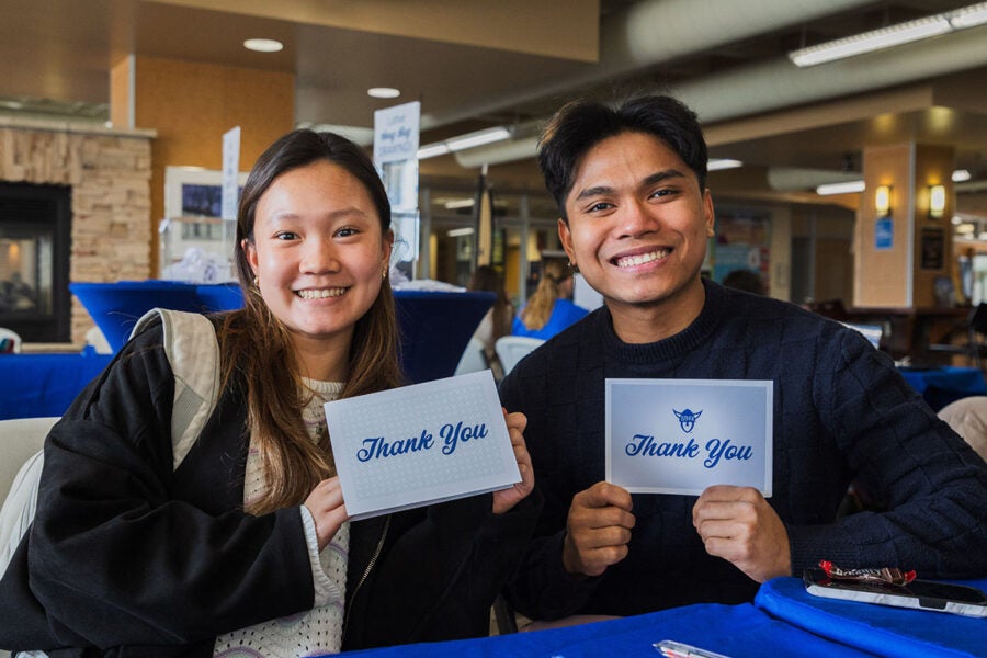 two students hold up thank you cards