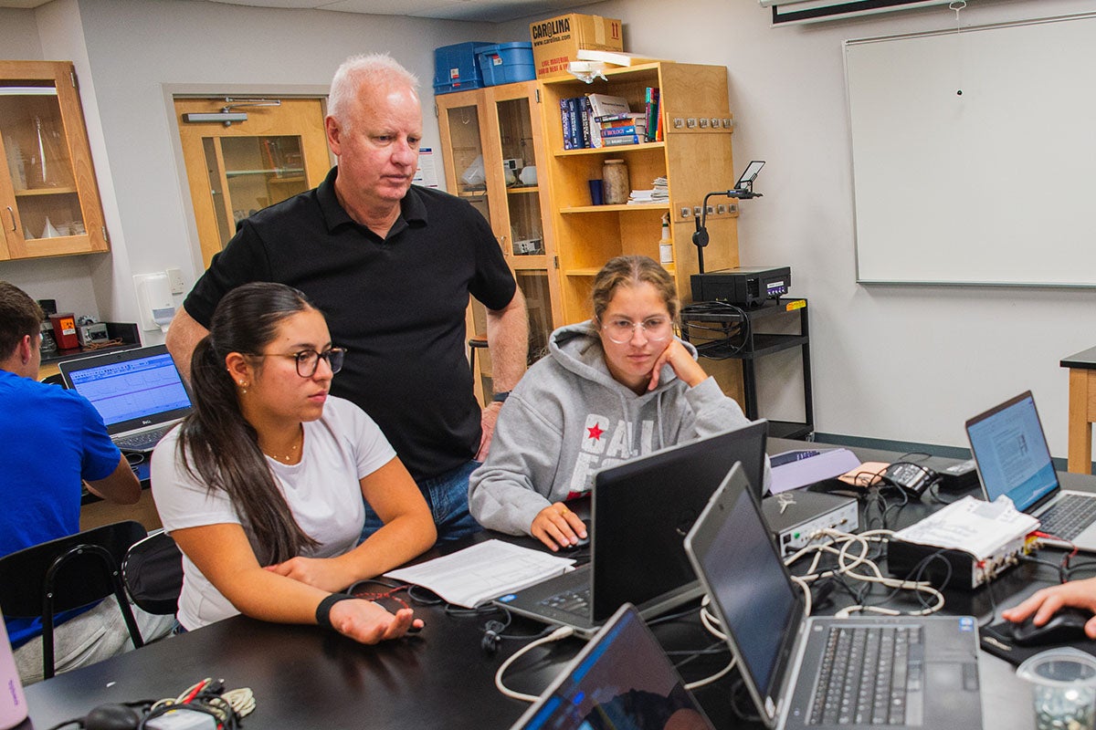 a professor and students at a table, looking at computers