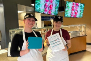 dining service workers hold up a stainless steel container at Oneota Market