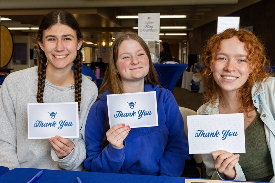 Three Luther students hold up thank you notecards