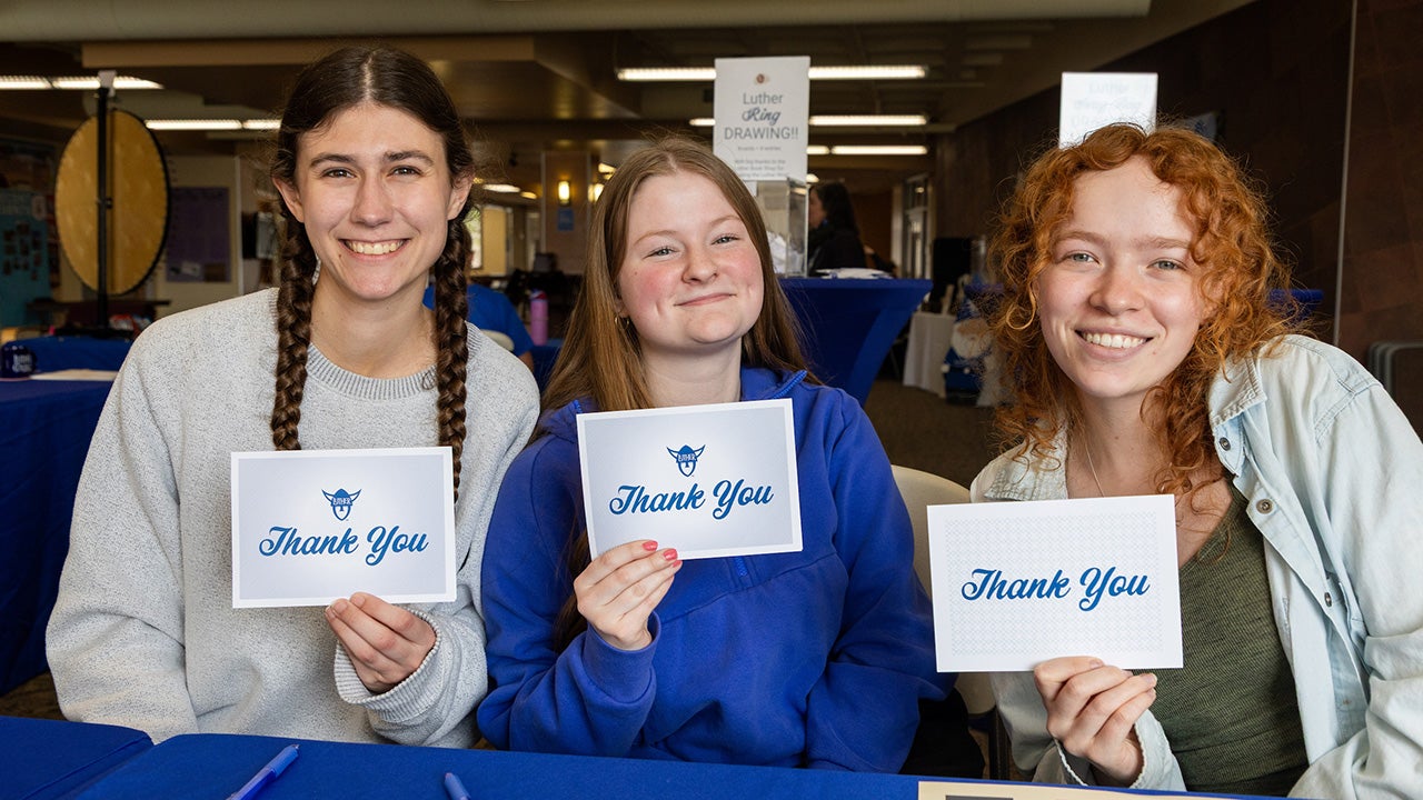 Three Luther students hold up thank you notecards