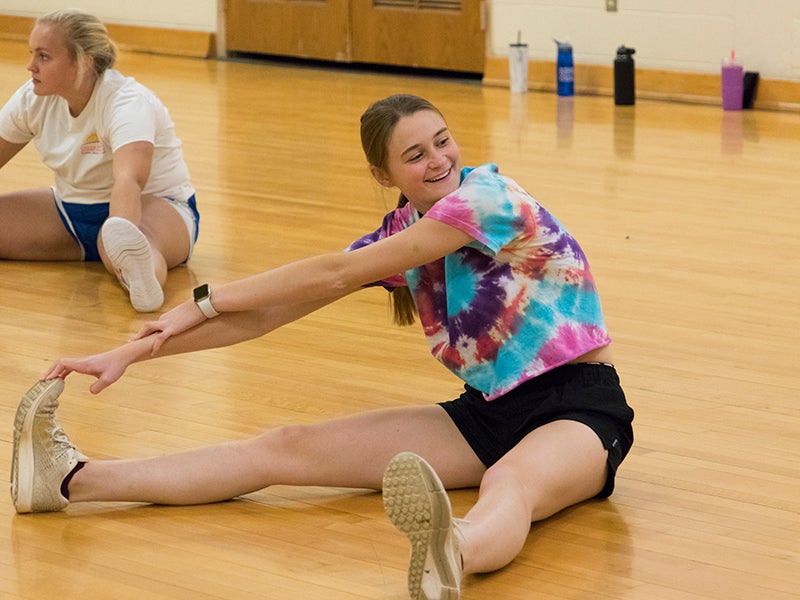 A student sits on the floor stretching her leg
