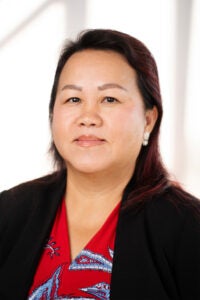 professional headshot of a woman wearing a red and blue patterned blouse and a black jacket.