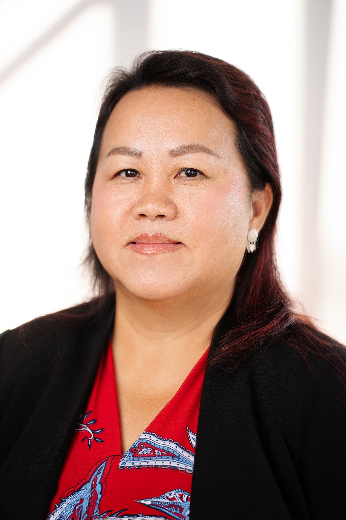 professional headshot of a woman wearing a red and blue patterned blouse and a black jacket.