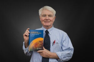 Chemistry professor John R. Jefferon holds a copy of the interdisciplinary biophysical chemistry textbook written by him.