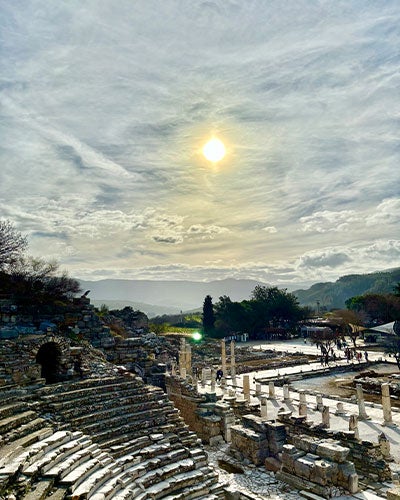 The ruins of an ancient city, including an amphitheater and columns with low bluffs or mountains in the distance
