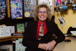 A person wearing a red shirt and black suit jacket sits at a desk