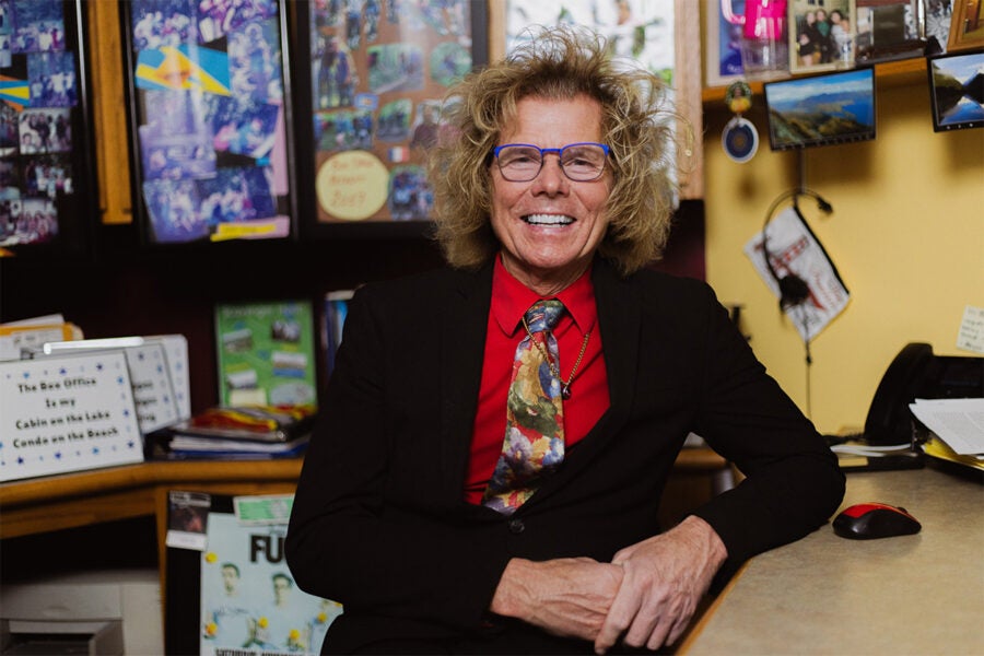 A person wearing a red shirt and black suit jacket sits at a desk