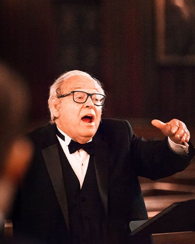 A man in a black tuxedo making a conducting gesture