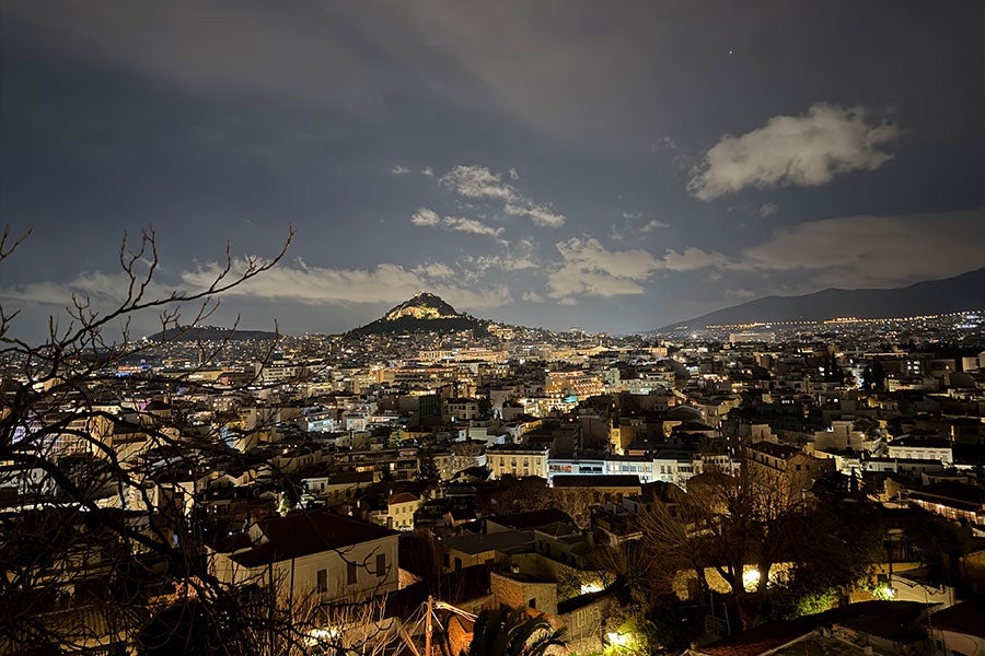 A cityscape at night with the silhouette of low mountains in the background