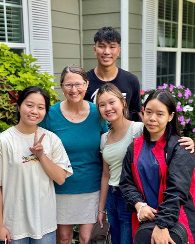 A group of five people posing in a friendly way together in front of a house
