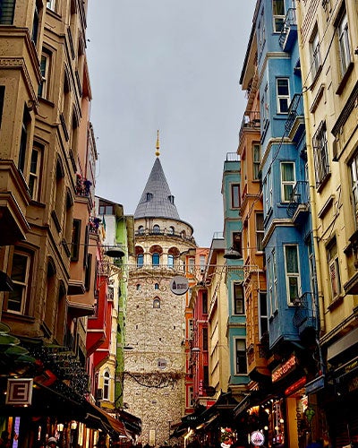 An alleyway of tall colorful buildings leading to a tall brick turreted building at the end of the alley
