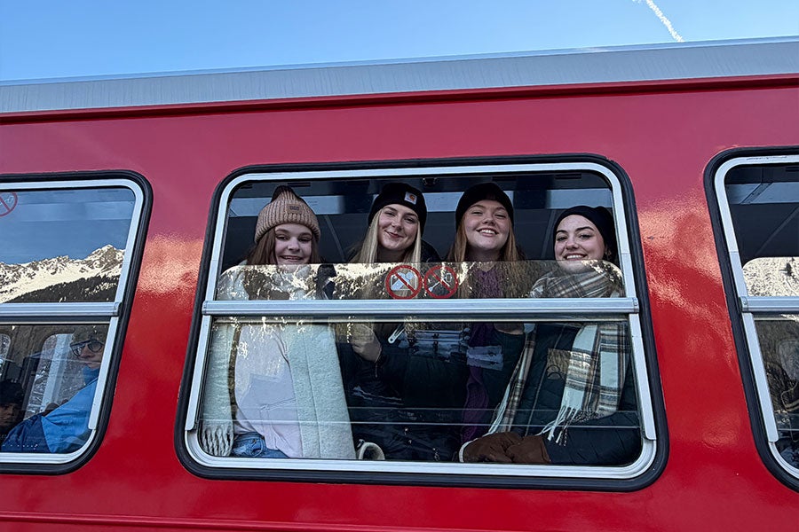 A close-up on a red bus with four women smiling through the window