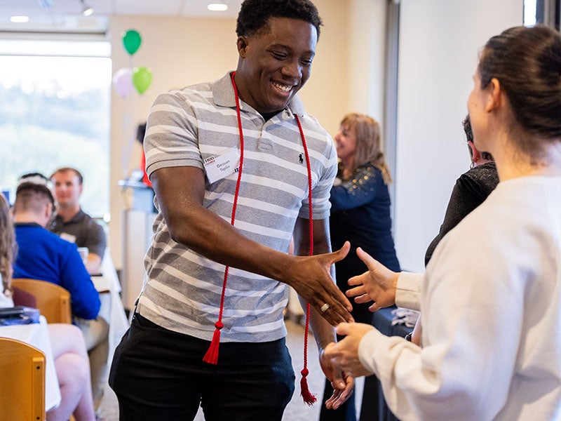 A student smiles and shakes hands at a banquet.