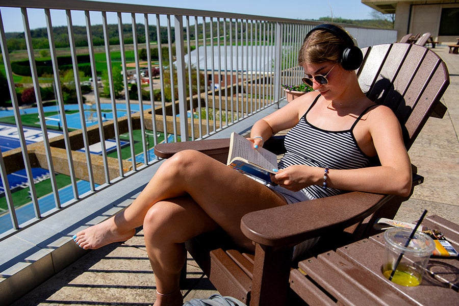 Student sunning herself in a deck chair reading with headphones on