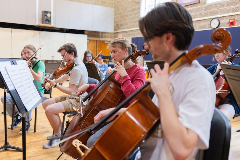 String players including cells and violins play their instruments in a rehearsal room.