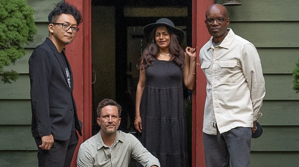 Members of the performance group American Patchwork Quartet gathered in front of a green, clapboard building with rend trim