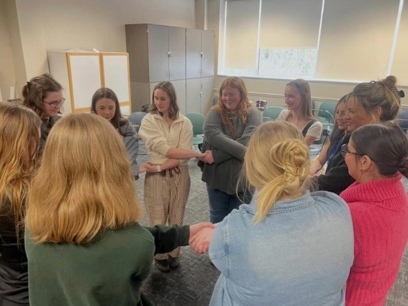 a group of students stands in a circle, holding hands with arms crossed