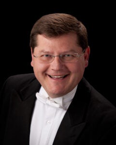 professional headshot of a choral conductor wearing a white bow tie, white shirt and black jacket
